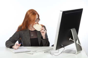Девушка одновременно ест и работает за компьютером.