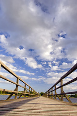 Long wooden plank bridge over lake and cloudy sky.