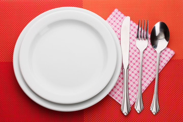 White empty plate with fork, spoon and knife on a red tablecloth