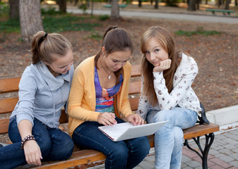 three pretty student girls in the park and surfing the internet