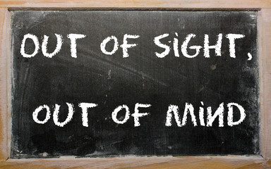 Proverb "Out of sight, out of mind" written on a blackboard