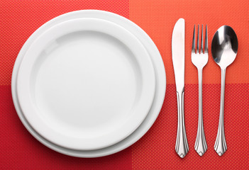 White empty plate with fork, spoon and knife on a red tablecloth