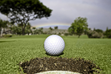 Golf ball at hole.  Rainbow and trees in the background.