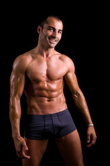 Fototapeta na wymiar Smiling muscular young man posing against black background