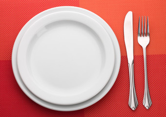White empty plate with fork and knife on a red tablecloth