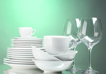 Clean plates, cups and glasses on green background
