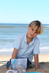 Little boy collecting starfish in a bucket on the beach