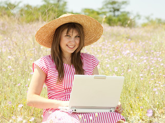 Beautiful brunette girl in hat at the park with computer.