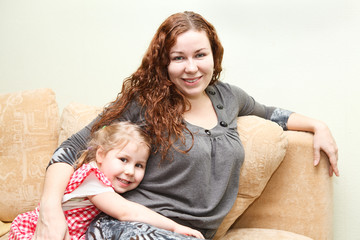 Mother and little daughter sitting and hugging on couch