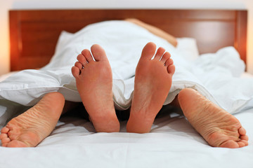 Two pairs of male and female feet seen from under the blanket
