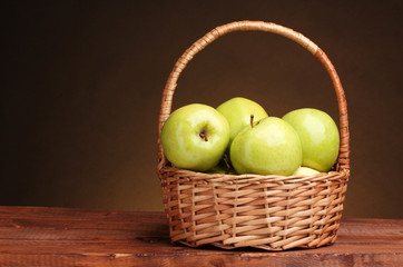 juicy green apples in basket on wooden table on brown background