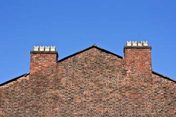 Old red brick wall with chimney pots against a clear blue sky