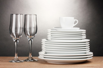 Clean plates, glasses and cup on wooden table on grey background