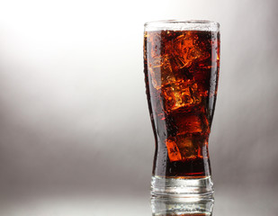 Glass of cola with ice on grey background