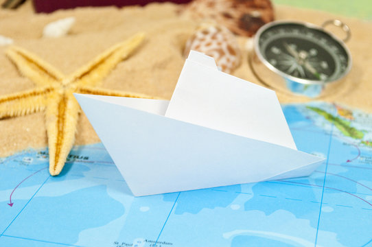 Weltkarte mit Papierschiff, Kompass, Seestern und Sand