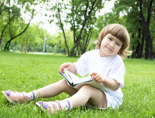 Portrait of little girl reading a book in the park