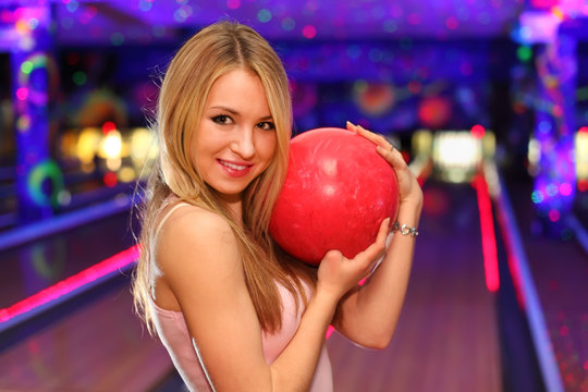 blonde girl stands and hugs red ball in bowling club