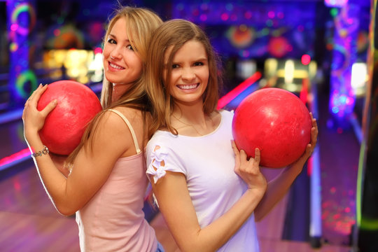 Two girls wearing white T-shirts stand and keep red ball