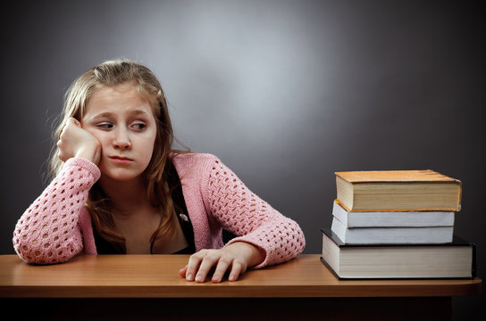 Unhappy schoolgirl with a stack of books