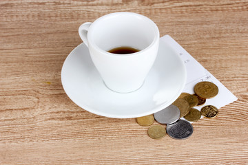 Empty cup of coffee with coins tip on wooden background