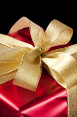 Golden gift bow on red, black background, close-up