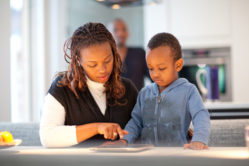 Kitchen setting with young black family playing with a tablet pc