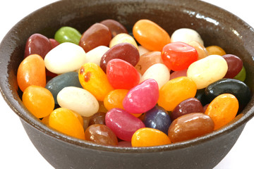 Colourful candies in a brown bowl on white background