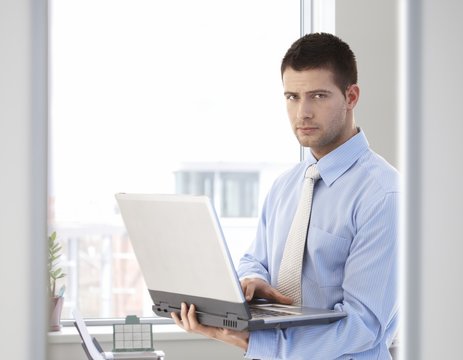 Young businessman standing with laptop in hand