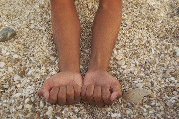 Man tanned hands compressed into cams on background stones beach