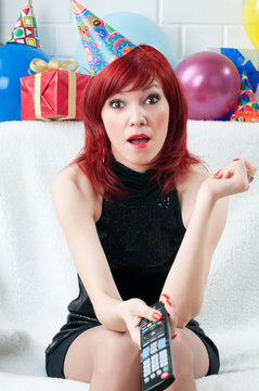 Surprised red-haired party woman sitting before TV