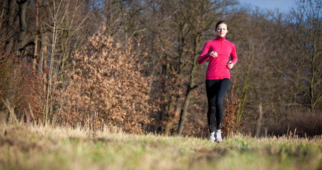Naklejka na ściany i meble Young woman running outdoors on a lovely sunny winter/fall day