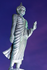 Back of walking Buddha statue in twilight tilted
