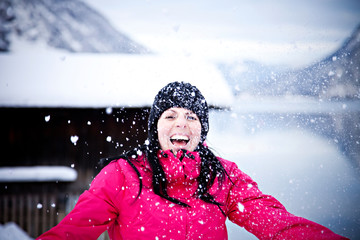 Lachende junge Frau in pinker Jacke hat Spaß im Schnee vor einer verschneiten Landschaft