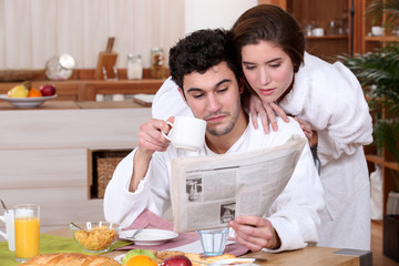 Young couple reading a newspaper at breakfast