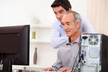 Young man teaching an elderly man computer skills