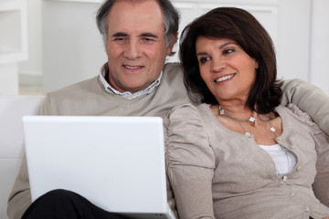 Middle-aged couple with laptop sat on sofa