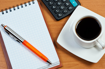 Coffee, notepad with pen and calculator on work-table.
