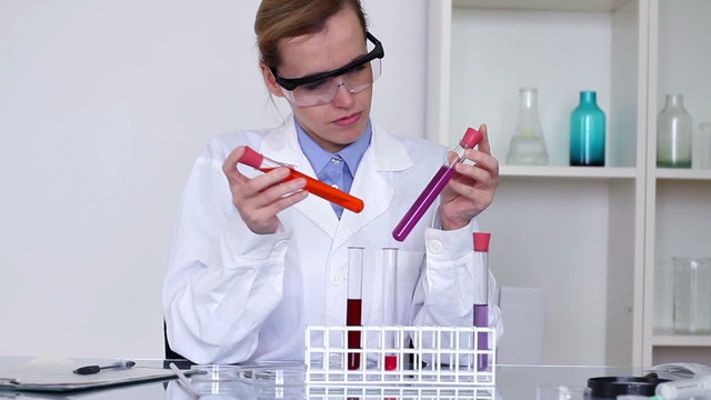 Female scientist comparing test tubes and writing results