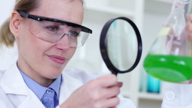 scientist with magnifying glass looking at erlenmeyer flask