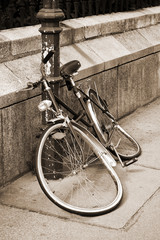 Abandoned damaged bicycle locked to an iron pillar on sidewalk