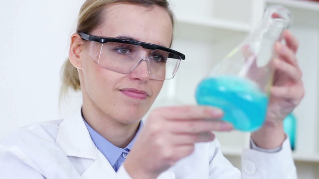 Female scientist mixing erlenmeyer flask with blue chemicals