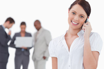 Smiling businesswoman on the phone with colleagues behind her