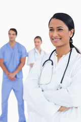 Fototapeta premium Smiling doctor with arms folded and colleagues behind her
