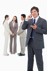 Salesman talking on cellphone with team behind him