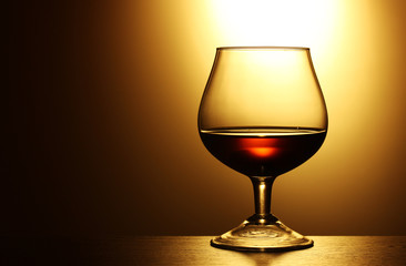Glass of cognac on yellow background