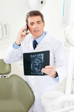 Zahnarzt telefoniert mit Röntgenbild in der Hand