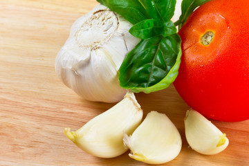 Garlic, tomato and basil on wooden board