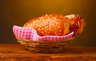 Baked bread in basket on wooden table on brown background