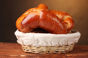 Baked bread in basket on wooden table on brown background