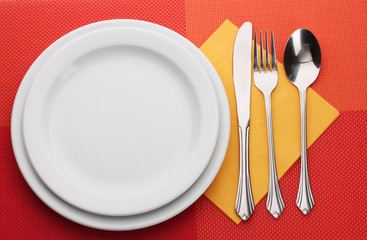 White empty plate with fork, spoon and knife on a red tablecloth